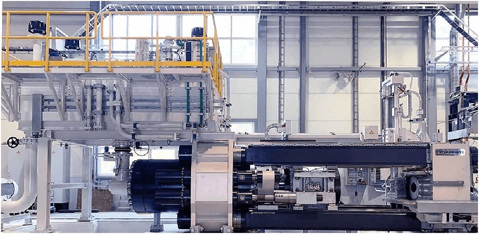Extrusion press line with steel framework and yellow safety railings inside a factory hall.
